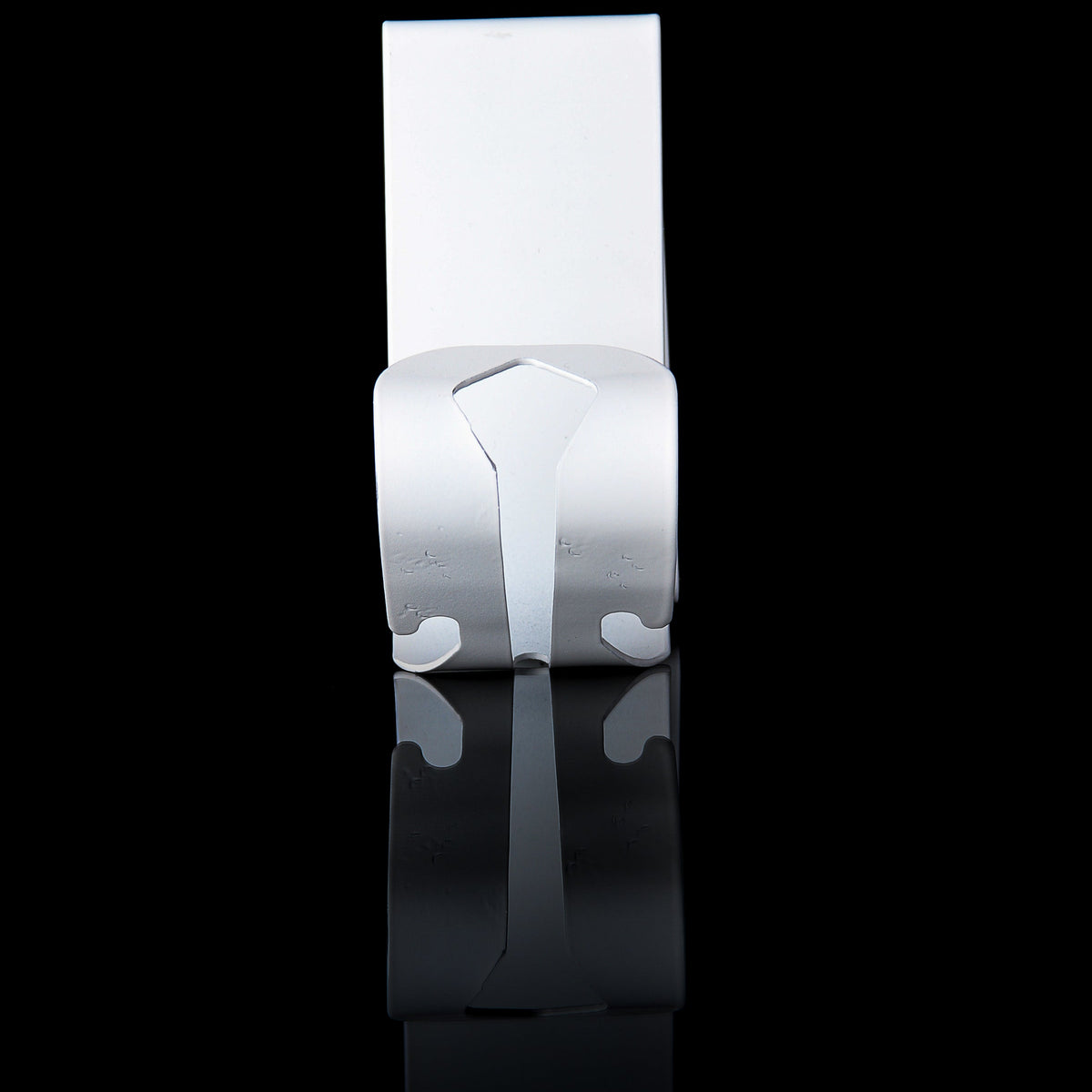 A polished silver metal wall hook with a geometric, sculptural design, shown against a solid black background with a clear reflection below.